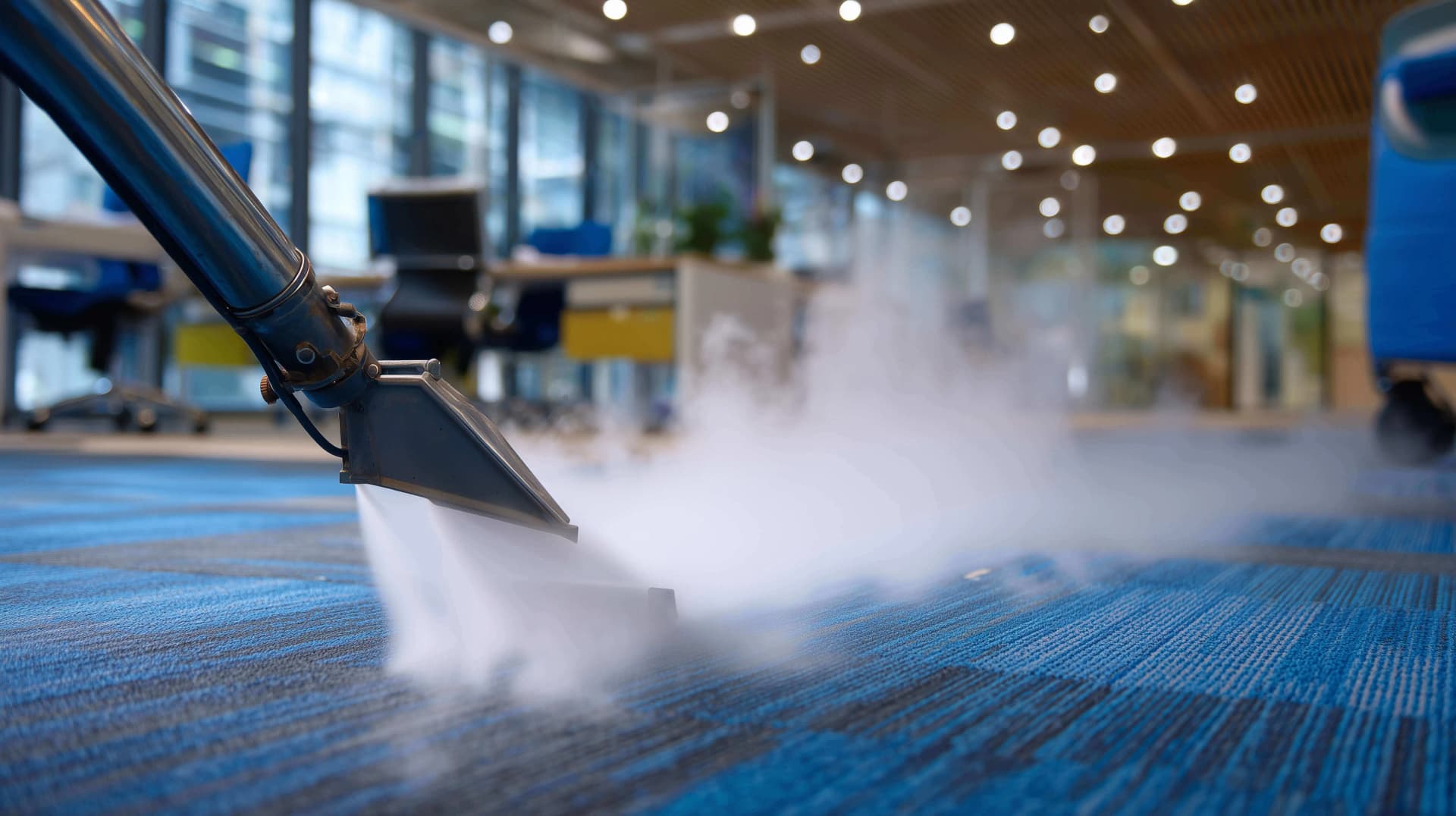 Steam carpet cleaning wand releasing hot steam over blue office carpet, representing professional commercial carpet cleaning services.