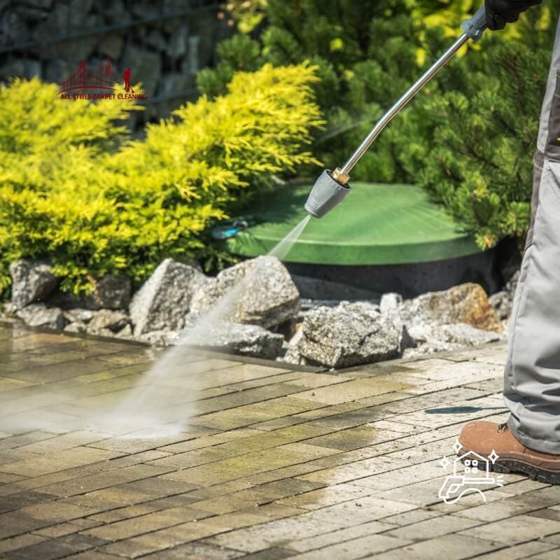 Technician power washing outdoor patio tiles in Bay Area backyard, removing built-up dirt and mildew with professional pressure washing equipment